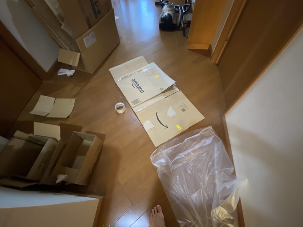 室内の廊下で段ボールを展開し、ガムテープとごみ袋を使って落ち葉ボックスの防水内張りを制作している様子。