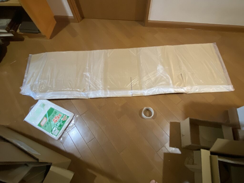 フローリングの上に展開した大きな段ボール板。防湿のために45Lごみ袋を貼り合わせ、落ち葉ボックスの内張りを作っている途中。