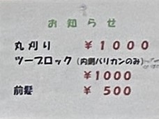 理容室の料金表を示すお知らせ掲示。 丸刈り1,000円、ツーブロック（内側バリカンのみ）1,000円、前髪カット500円と、格安料金で利用できる床屋の価格表示。手軽にカットできるリーズナブルな理髪店として、節約志向の男性やシニア層にも人気。