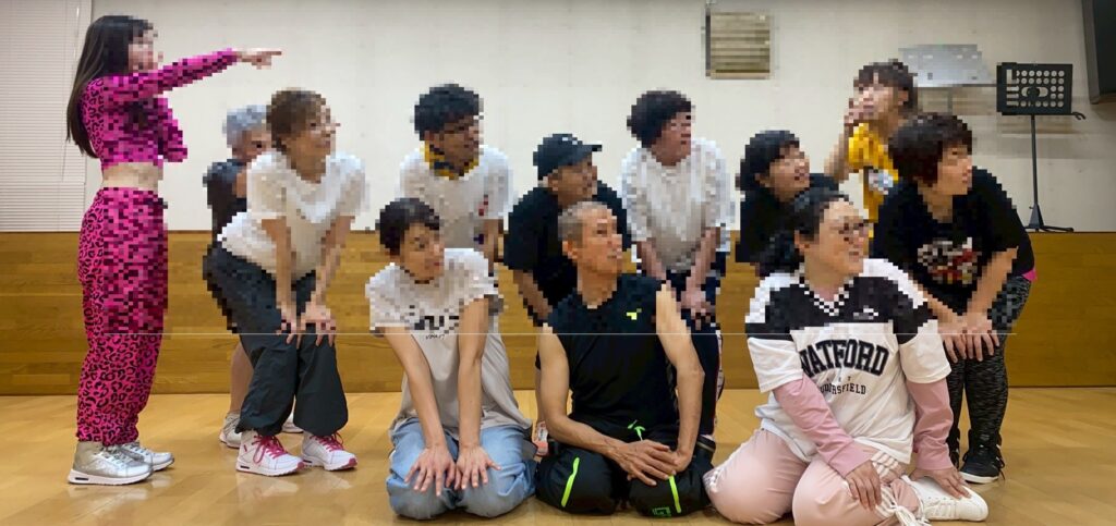 ZUMBAサークルのメンバーがスタジオで集合ポーズをとっている様子。カラフルなウェアを着たインストラクターが指をさし、笑顔で盛り上がる参加者たち。運動後の充実した雰囲気が伝わるグループ写真