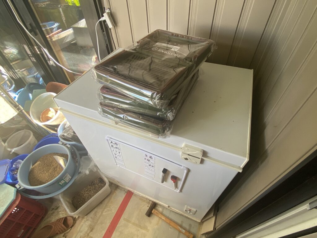新品のZak-Storage折りたたみコンテナを3個重ね、ビニール包装のまま冷凍庫の上に置いた状態。これから使用するための準備が整っている。