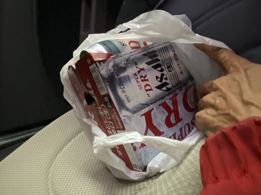 「MOS美への誕生日プレゼントとして、車の座席に置かれたアサヒスーパードライの6缶パック。白いビニール袋から赤と銀のパッケージがのぞき、プレゼントを手渡す瞬間を思わせる一枚。」