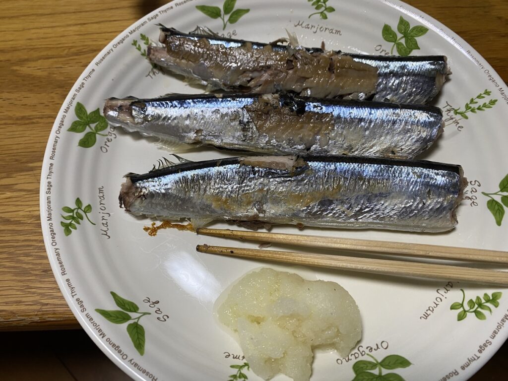 皿に盛られた焼きサンマ3尾と大根おろし。脂がのった秋刀魚の銀色の皮が輝き、箸が添えられている和食の一品。