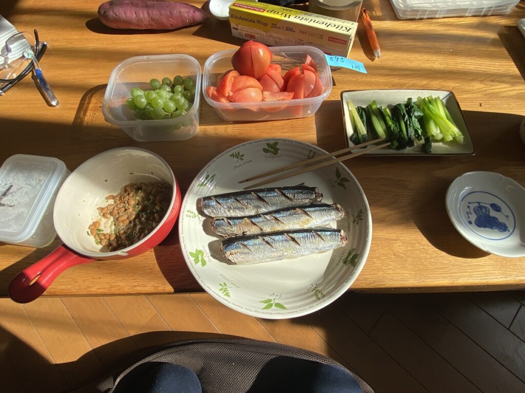 「トマト、小松菜のおひたし、焼きサンマ、納豆、ぶどうを組み合わせた栄養バランスの良い和食メニューの食卓。」