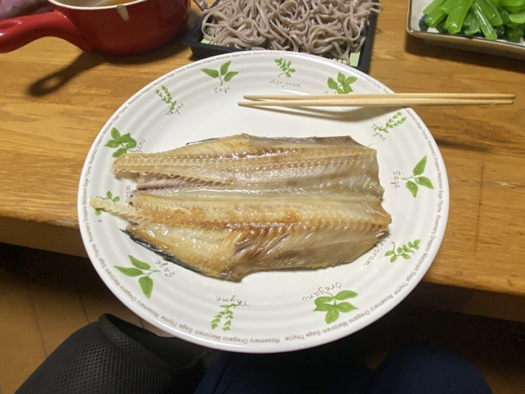香ばしく焼き上げたホッケの開きが、白いハーブ柄の皿に盛り付けられた和食の一品。 身はふっくらと脂がのり、ほどよい塩味でご飯やそばとの相性も抜群。 高たんぱく・低脂質で、ダイエット中や健康志向の食卓にもおすすめの焼き魚メニュー。