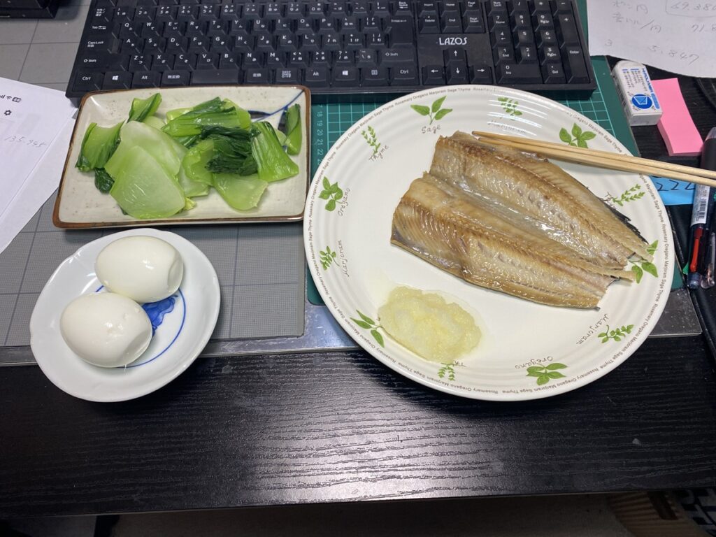 夕食の食卓。焼いたホッケの開きと大根おろし、チンゲンサイのおひたし、ゆで卵2個を並べた和定食。冷凍庫から取り出して焼いたホッケがメインで、チンゲンサイは初めて購入しておひたしにした一品。小松菜・ほうれん草と並ぶ定番野菜として比較検討中。