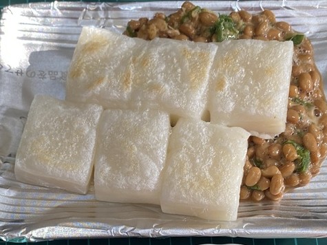 香ばしく焼いた切り餅を納豆にのせた納豆もちのアップ。 一度くっつくと離れないほどもちもちで、納豆の粘りと香りが食欲をそそる。